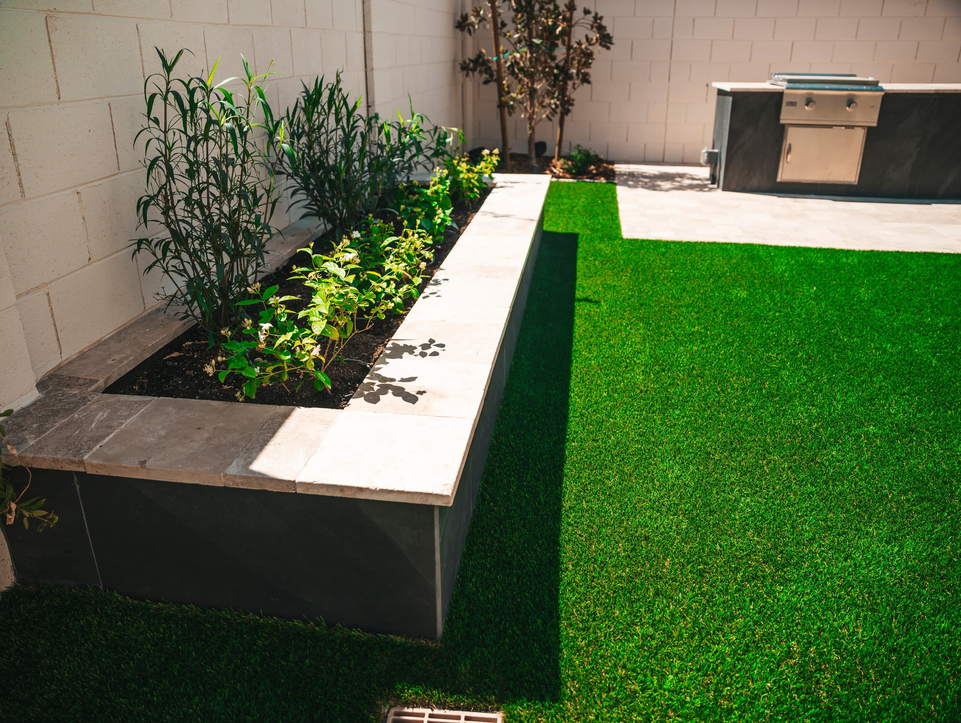 Raised planter beside a turf lawn, with a built-in grill island in the corner, in a Gilbert backyard