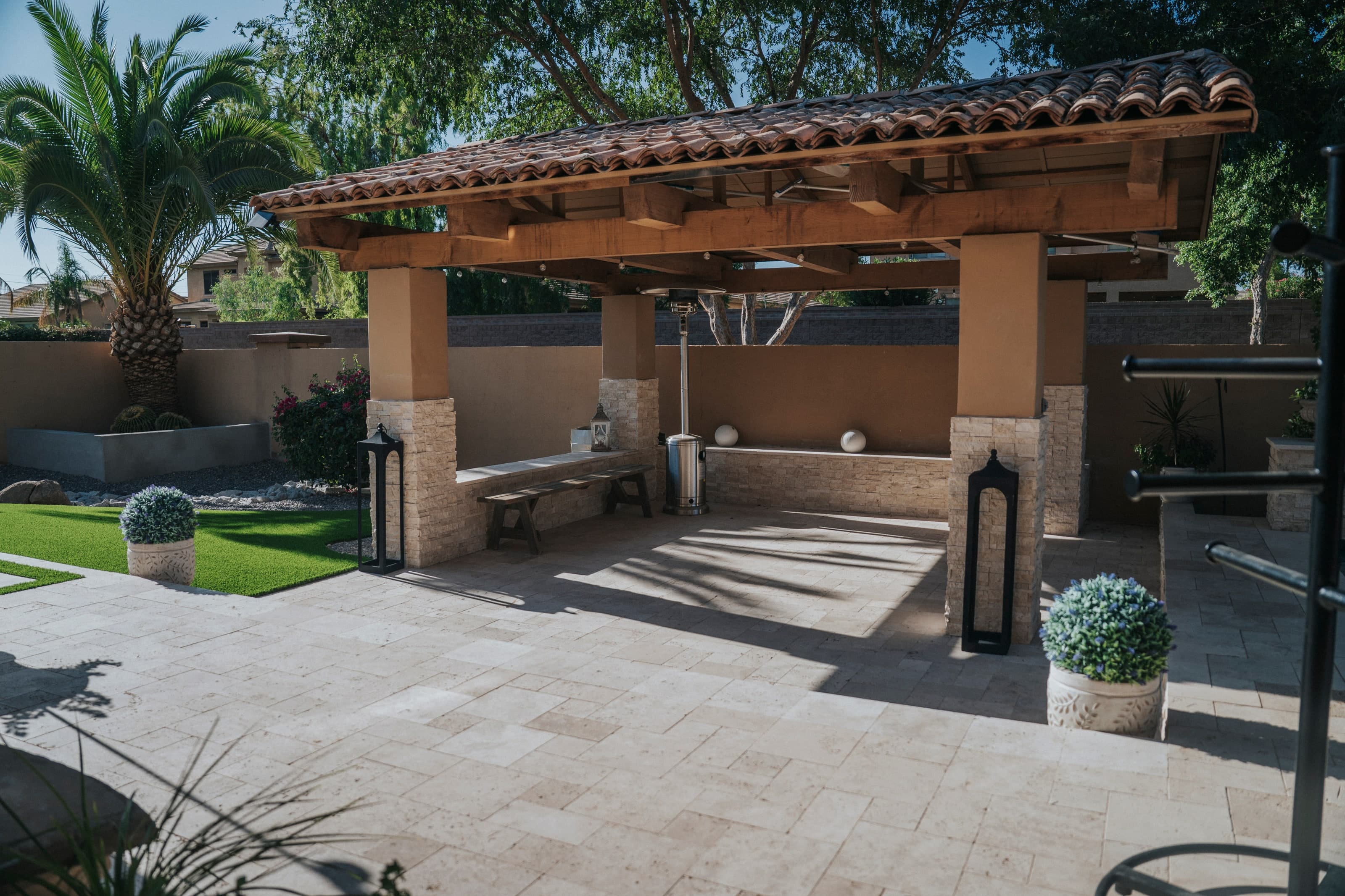 Tiled stone ramada with built-in bench seating, lanterns, and string lighting in a Chandler backyard
