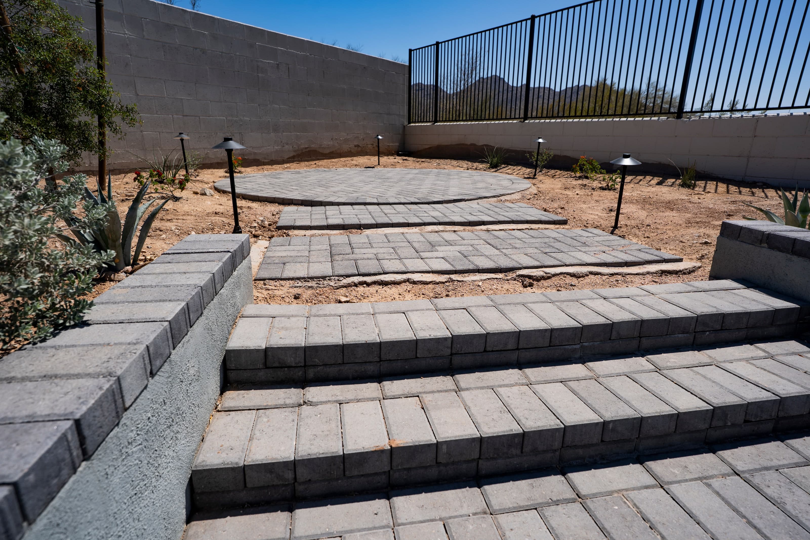 Paver steps and a circular patio under construction in a Queen Creek backyard, with landscape lighting roughed in before turf and planting