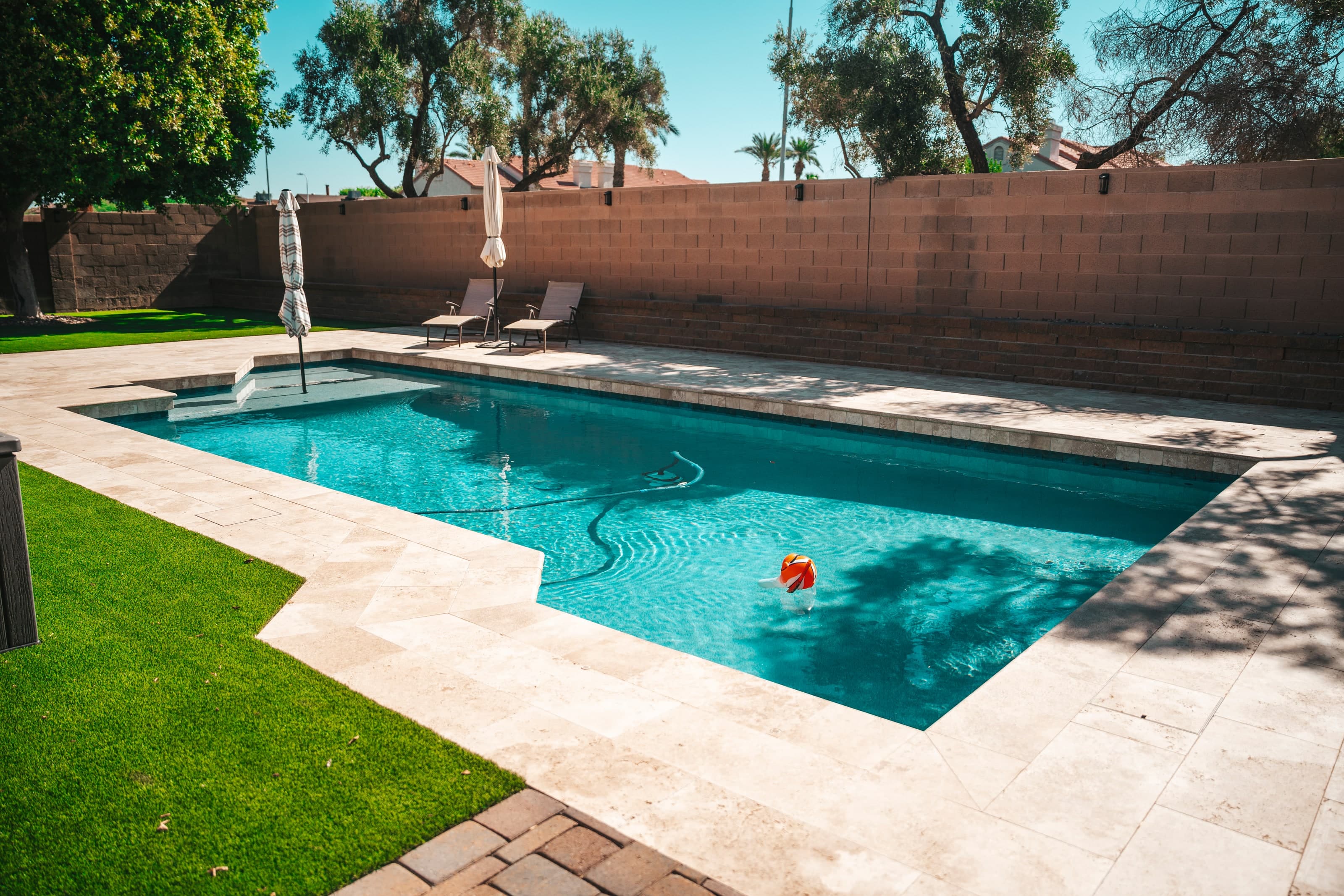 Backyard pool with travertine decking, lounge chairs, and mature trees in Chandler